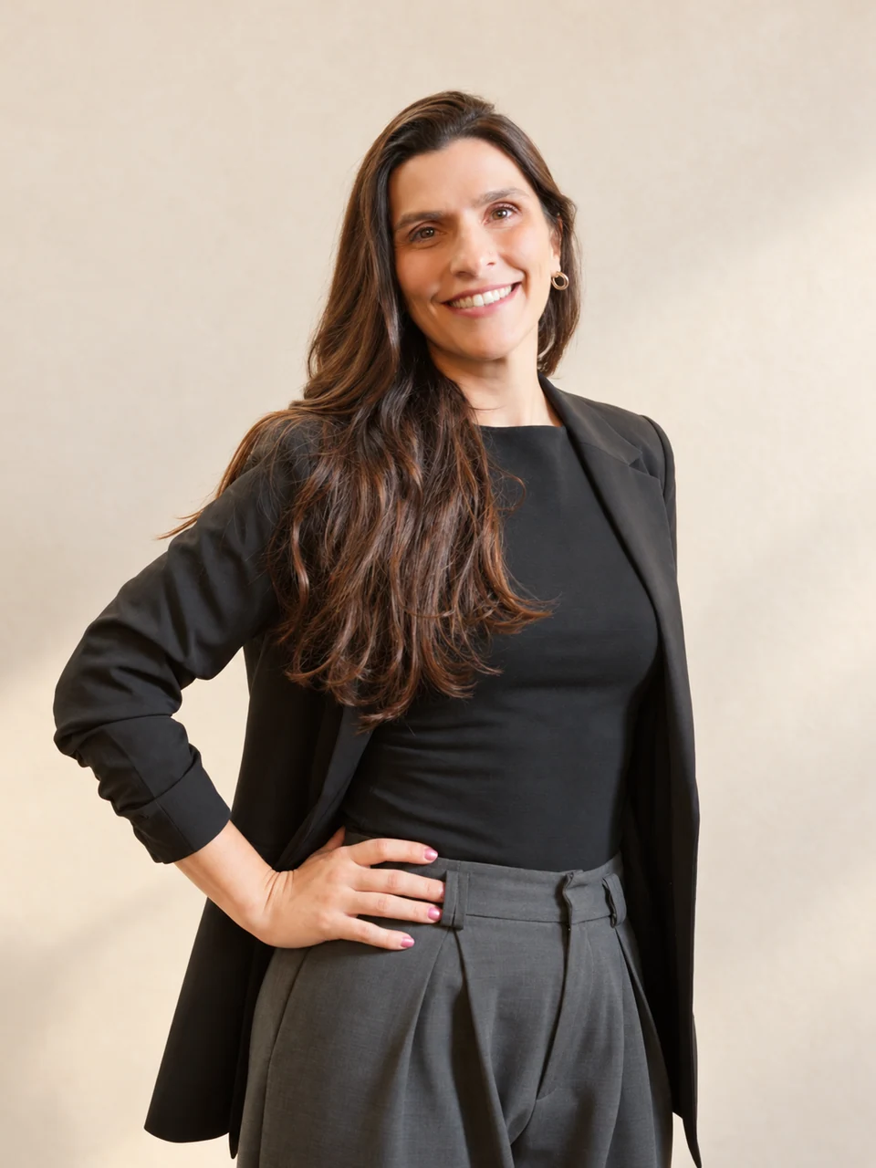 Dra. Gabi Chefaly sorrindo, em pé, de blazer preto e com uma das mãos na cintura.